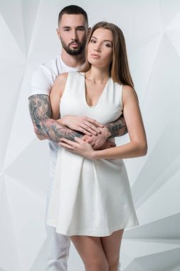 Kadının omuz üzerinden ellerini tutarak ve kamera için seyir kadınla genç casual çift. Beyaz arka plan üzerinde