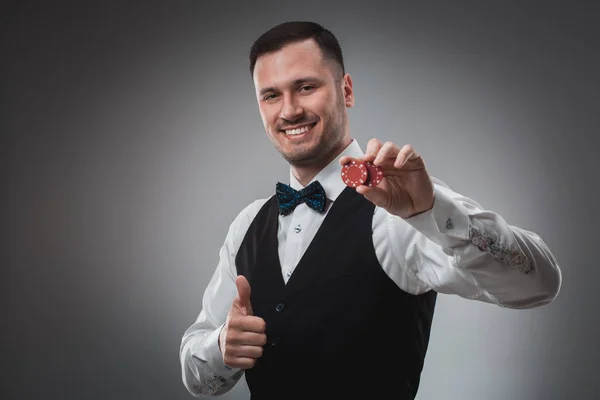 Молодий чоловік у сорочці та жилеті показує свої покерні чіпи, студійний знімок — стокове фото