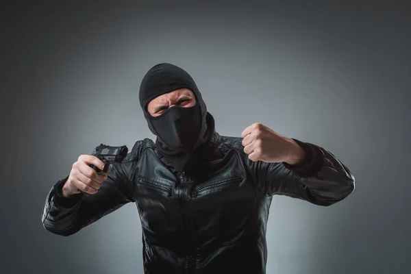 Masked robber with gun, looking into the camera.