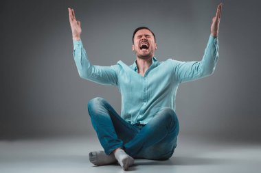 Gri arka plan üzerinde izole kaldırdı elleriyle bir katta oturan yakışıklı genç adam