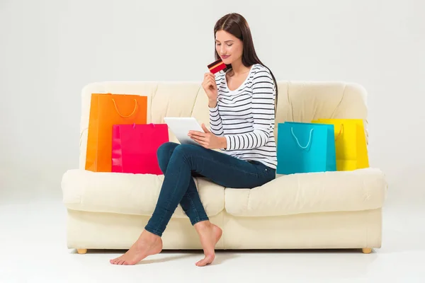 Молода жінка з кредитною карткою купує сидячи на дивані з паперовими пакетами та новим одягом — стокове фото