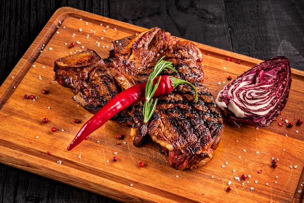 Medium rare grilled steak on rustic cutting board with rosemary and spices , dark rustic wooden background, top view — Stock Photo, Image