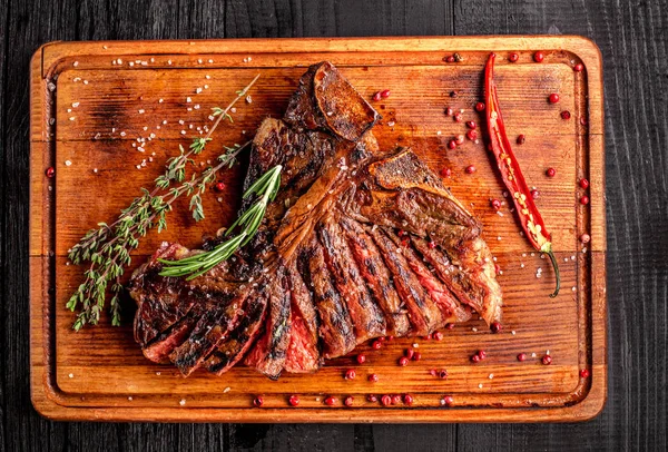 Middelgrote zeldzame gegrilde steak gesneden op rustieke snijplank met rozemarijn en specerijen, donkere rustieke houten achtergrond, bovenaanzicht — Stockfoto