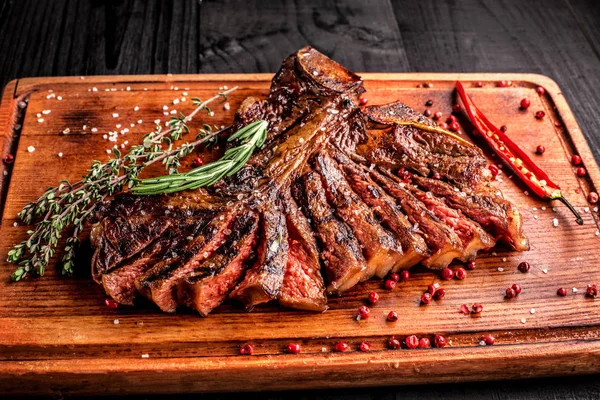 In Scheiben geschnittenes mittelseltenes gegrilltes Steak auf rustikalem Schneidebrett mit Rosmarin und Gewürzen, dunkler rustikaler Holzhintergrund, Draufsicht — Stockfoto