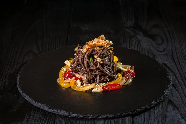 Χυλοπίτες από φαγόπυρο Noodles φαγόπυρου κίτρινο και κόκκινο πιπέρι, βότανα. Παν-Ασιατική κουζίνα. Στο πέτρινο δίσκο στο σκοτεινό ξύλινο τραπέζι. — Φωτογραφία Αρχείου