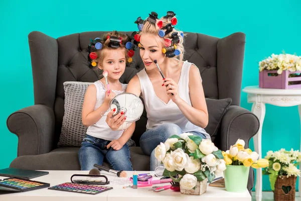 Mom and daughter in the studio on the sofa in the curlers make up and have fun