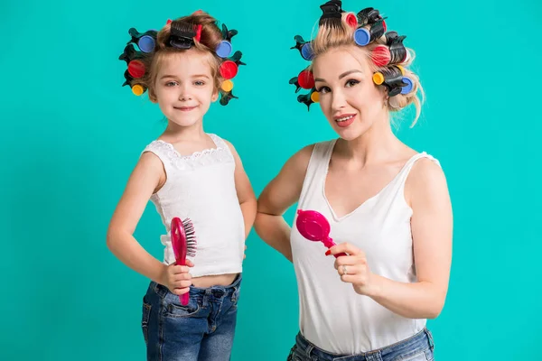 Mutter und kleine Tochter in Lockenwicklern auf türkisfarbenem Hintergrund im Studio — Stockfoto