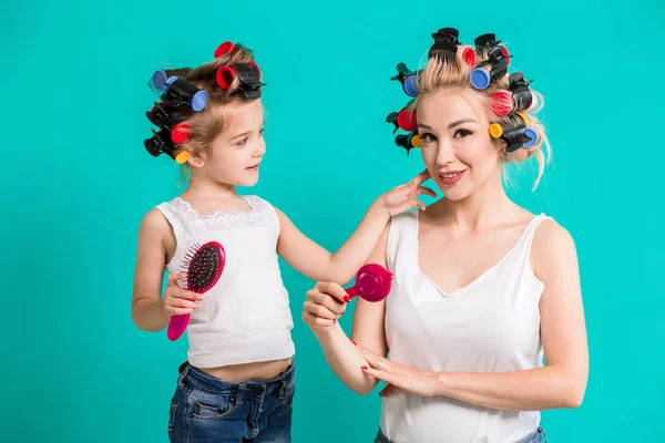 Mãe e pequena filha em encrespadores de cabelo em um fundo turquesa no estúdio — Fotografia de Stock