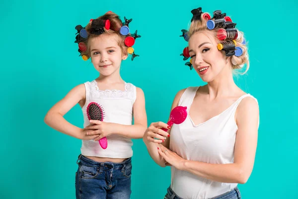 Mother and little daughter in hair curlers on a turquoise background in the studio