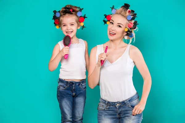 Mutter und kleine Tochter in Lockenwicklern auf türkisfarbenem Hintergrund im Studio — Stockfoto