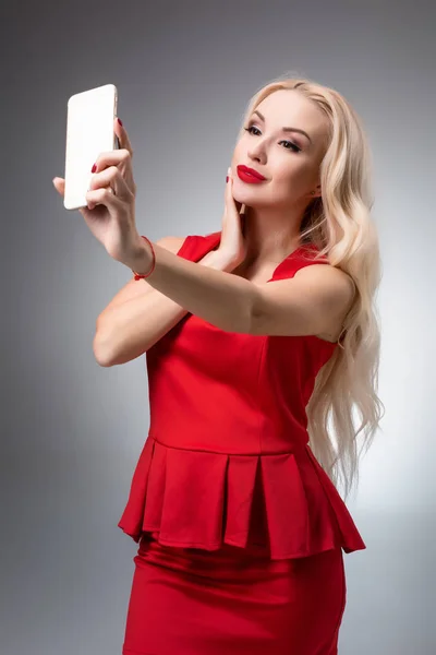 밝은 배경에 빨간 드레스에 selfie 하 고 아름 다운 성공 웃는 여자의 초상화 — 스톡 사진