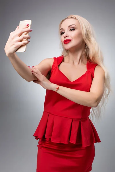 밝은 배경에 빨간 드레스에 selfie 하 고 아름 다운 성공 웃는 여자의 초상화 — 스톡 사진