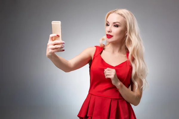 Porträt eines schönen erfolgreichen lächelnden Mädchens beim Selfie im roten Kleid auf hellem Hintergrund — Stockfoto