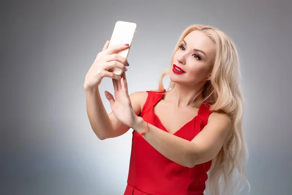 Retrato de uma bela menina sorridente bem sucedida fazendo selfie em vestido vermelho no fundo claro — Fotografia de Stock