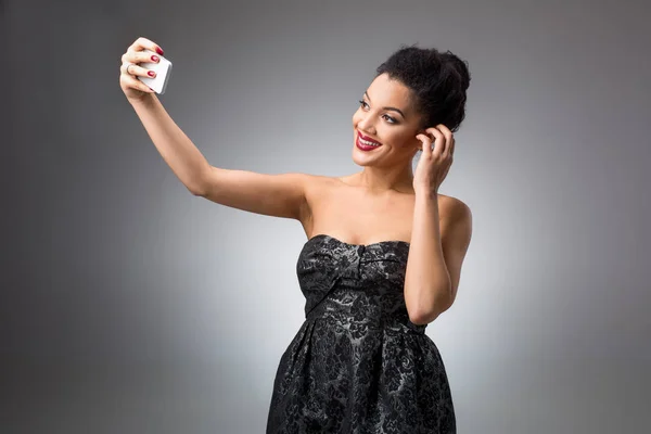 Portrét krásné úspěšné usmívající se holka dělá selfie v černých šatech na světlé pozadí — Stock fotografie