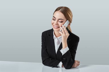 çekici esmer kadın siyah bir takım elbise giymiş bir ofiste masada oturuyor.