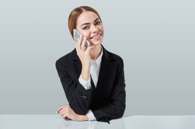 çekici esmer kadın siyah bir takım elbise giymiş bir ofiste masada oturuyor.