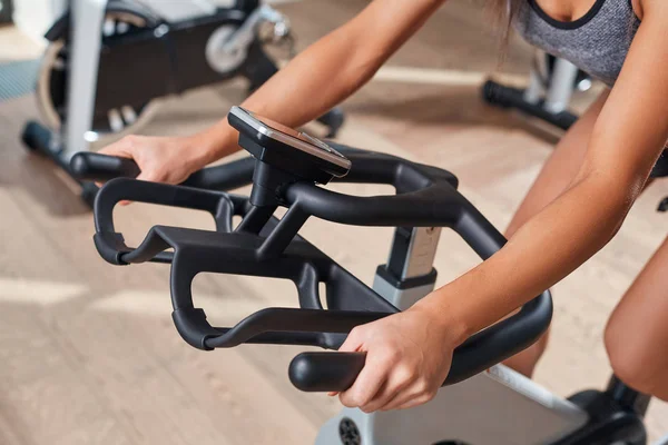 Mujer manos en una barra de bicicleta estacionaria el gimnasio — Foto de Stock