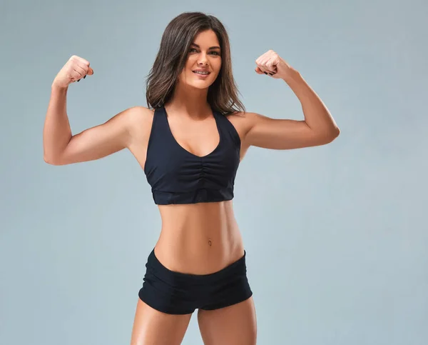 Los deportes y hermosa joven sobre un fondo gris. La encantadora chica con una figura deportiva y una hermosa sonrisa . — Foto de Stock