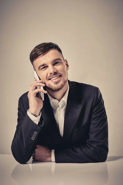 Красивий молодий чоловік розмовляє по мобільному телефону, сидячи на своєму робочому місці в офісі — стокове фото