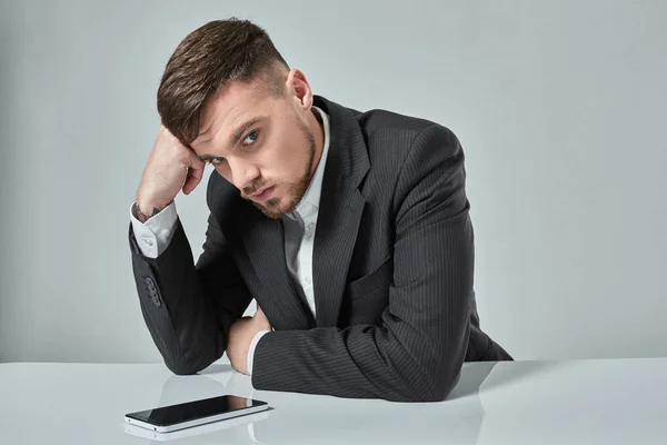 Retrato de un hombre caucásico joven atractivo usando el teléfono celular mientras está sentado en la mesa de la oficina . —  Fotos de Stock