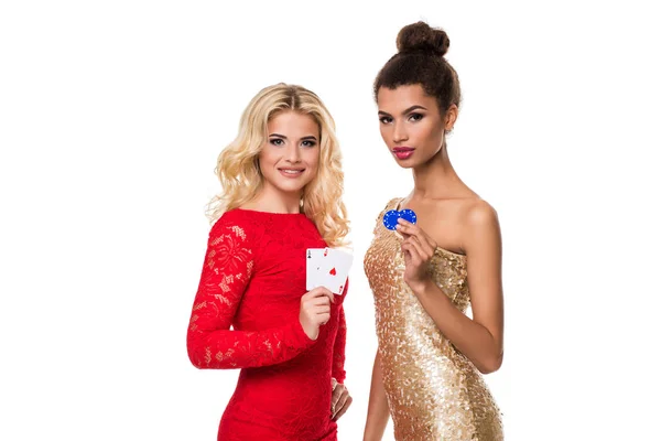 Krásná Africká žena a kavkazských mladá žena s dlouhou světle blond vlasy v večerní oblek. Drží, hrací karty a čipy. Izolovaný. Poker — Stock fotografie