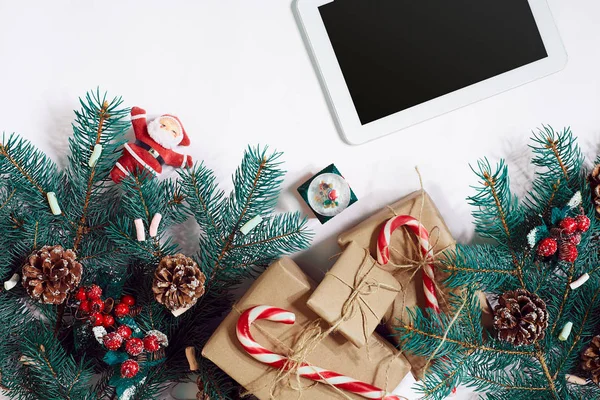 Christmas online shopping background. Tablet screen with copy space, spruce branches, gifts on white background.