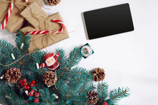 Christmas online shopping background. Tablet screen with copy space, spruce branches, gifts on white background.