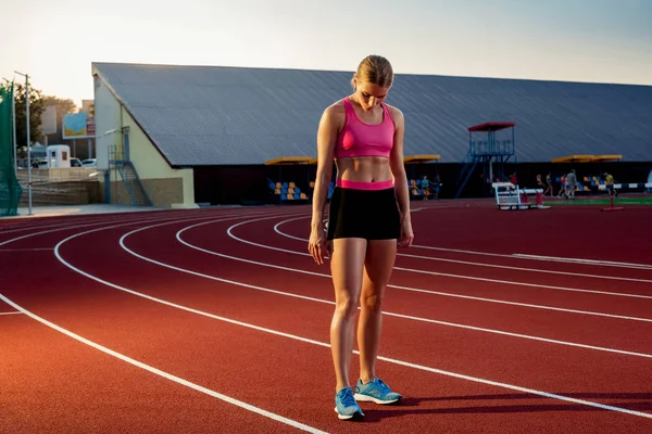 Imagen de la hermosa joven corredora europea o velocista de pie en la pista de estadio al aire libre, sintiéndose agotada después del sprint o maratón . — Foto de Stock