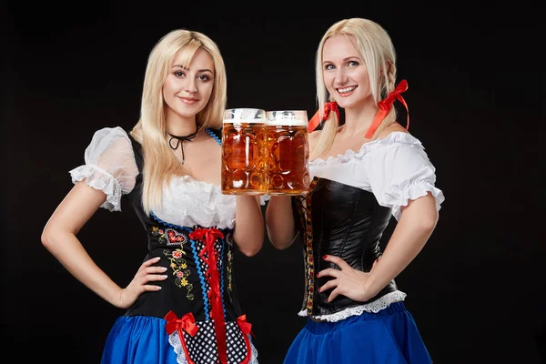 Дві красиві блондинки тримають келихи пива в руках і стоять на чорному тлі в студії . — стокове фото