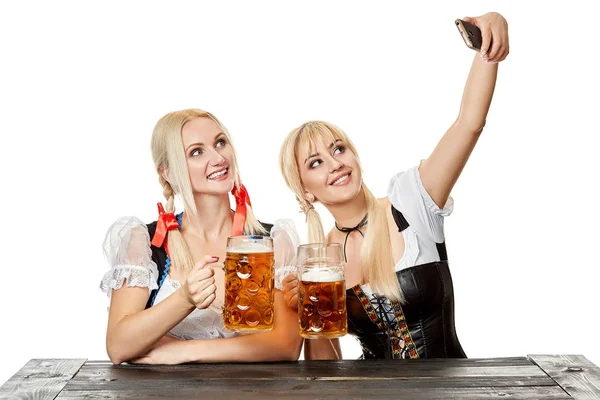 Twee mooie vrouwen die houden van een glas bier tijdens de vergadering op een houten tafel op een witte achtergrond in de studio — Stockfoto
