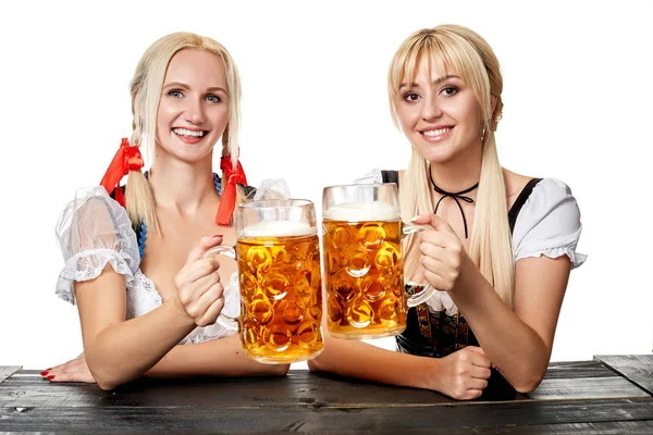 Due belle donne che tengono in mano un bicchiere di birra mentre siedono a un tavolo di legno su uno sfondo bianco in studio — Foto Stock
