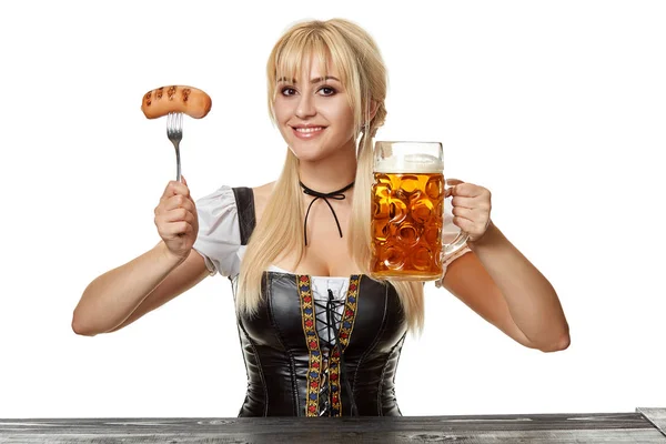 Beierse jongedame in dirndl zittend aan tafel met bier op witte achtergrond — Stockfoto