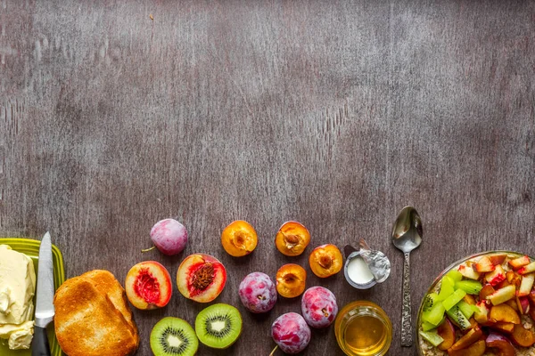 Harina de avena con ciruelas, kiwi y melocotón, tostadas con mantequilla y miel sobre una mesa de madera. El concepto de un desayuno saludable — Foto de Stock