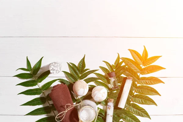 Spa set with towel and soap on white wooden background with green leaves. Sun flare — Stock Photo, Image
