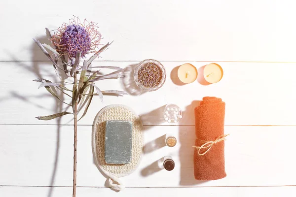 Beyaz ahşap zemin üzerinde kuru çiçek spa set deniz tuzu, uçucu yağ, sabun ve havlu ile süslenmiş. Güneş parlaması