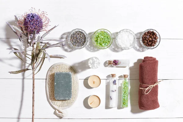 Beyaz ahşap zemin üzerinde kuru çiçek spa set deniz tuzu, uçucu yağ, sabun ve havlu ile süslenmiş