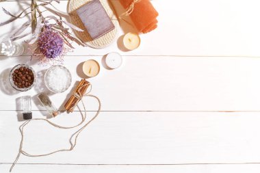 Beyaz ahşap zemin üzerinde kuru çiçek spa set deniz tuzu, uçucu yağ, sabun ve havlu ile süslenmiş. Güneş parlaması