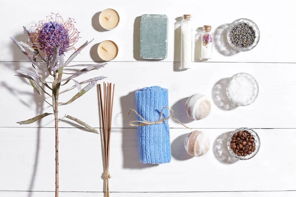 Beyaz ahşap zemin üzerinde kuru çiçek spa set deniz tuzu, uçucu yağ, sabun ve havlu ile süslenmiş