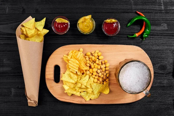 Blick auf Bierglas und Snacks mit Soße auf schwarzem Holztisch. — Stockfoto