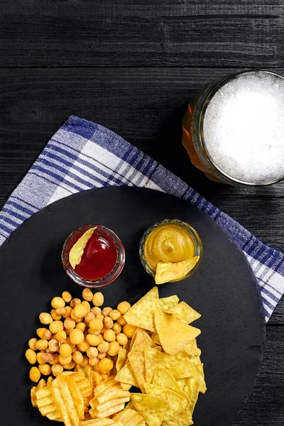 Blick auf Bierglas und Snacks mit Soße auf schwarzem Holztisch. — Stockfoto