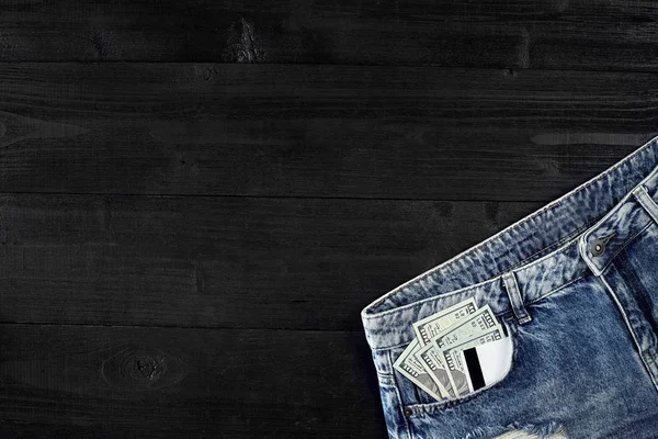 Dollari e carte in tasca jeans su sfondo nero in legno — Foto Stock