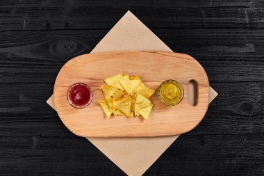 Siyah ahşap masa üzerinde hardal ve domates soslu tortilla cips. Üstten Görünüm