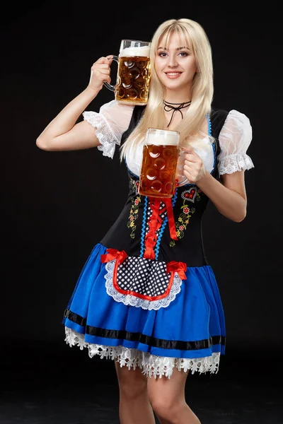 Young sexy woman wearing a dirndl with two beer mugs on black background. — Stock Photo, Image