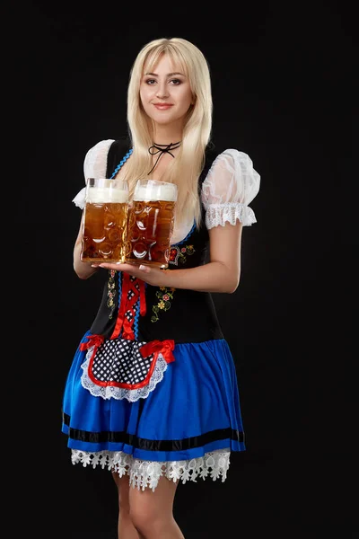 Young sexy woman wearing a dirndl with two beer mugs on black background. — Stock Photo, Image