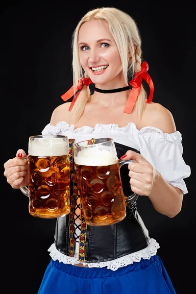 Wanita seksi muda mengenakan dirndl dengan dua gelas bir di latar belakang hitam . — Stok Foto