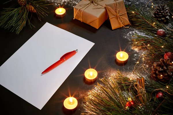 Christmas toys, burning candles and notebook lying near green spruce branch on black background top view. Space for text — Stock Photo, Image