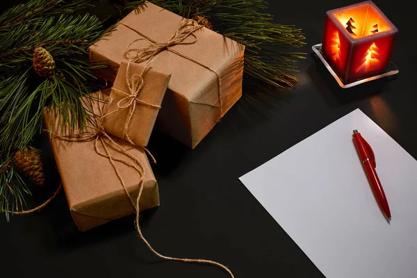 Christmas gifts and notebook lying near green spruce branch on black background top view. Space for text — Stock Photo, Image