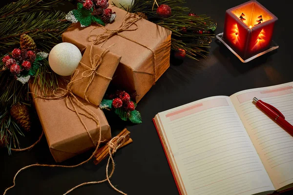 Christmas gifts and notebook lying near green spruce branch on black background top view. Space for text — Stock Photo, Image