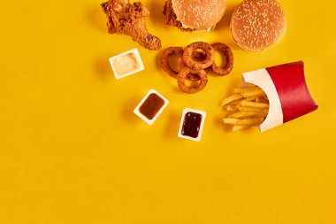 Fast food yemek üstten görünüm. Patates kızartması, hamburger, Sarı zemin üzerine mayonez, ketçap soslar.